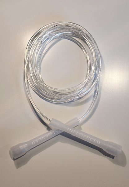 A coiled transparent jump rope with clear handles, displayed on a light gray surface. The handles feature the brand name 'INFLOENCED' printed on them.