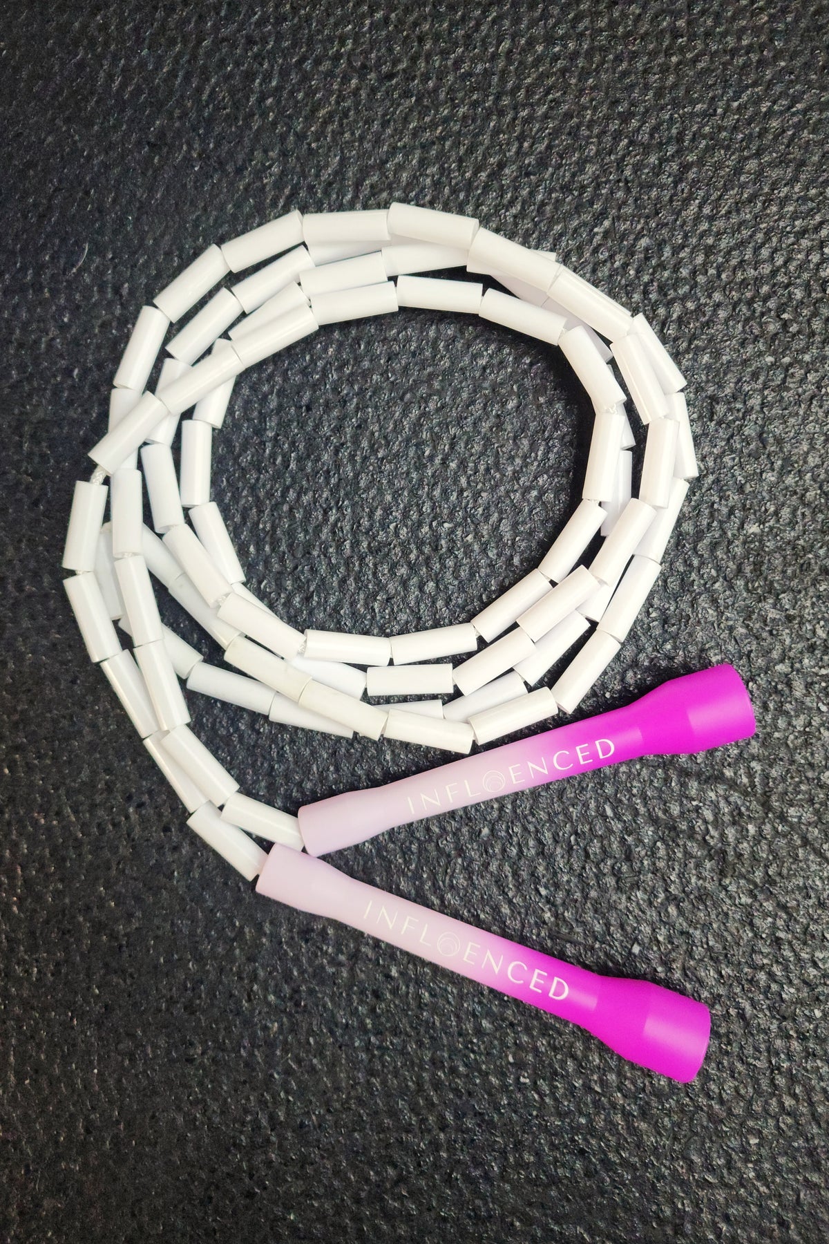 A white and pink jump rope coiled on a dark textured surface, with bright pink handles printed with the brand name Infloenced