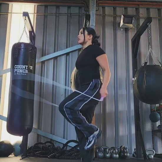 a girl skipping in a boxing gym practicing footwork with a white and pink pvc jump rope