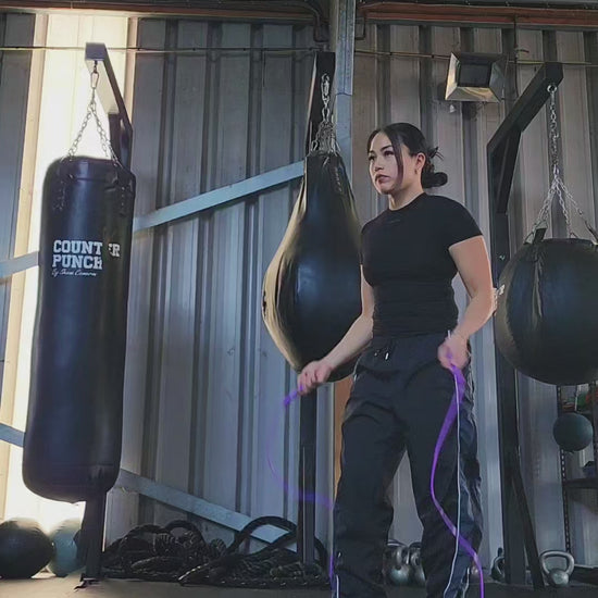 a girl skipping in a boxing gym practicing footwork with a purple and blue pvc jump rope