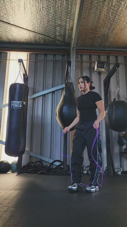 a girl skipping in a boxing gym practicing footwork with a purple and blue pvc jump rope