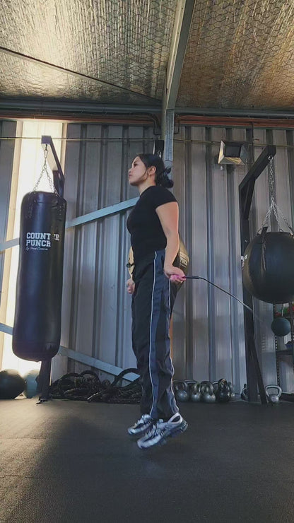 a girl skipping in a boxing gym practicing footwork with a black and pink pvc jump rope